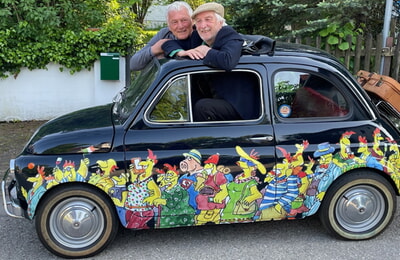 Cartoonist Peter Gaymann und Musik-Kabarettist Josef Brustmann schauen aus einem Auto mit Hühner-Cartoons von Peter Gaymann. 